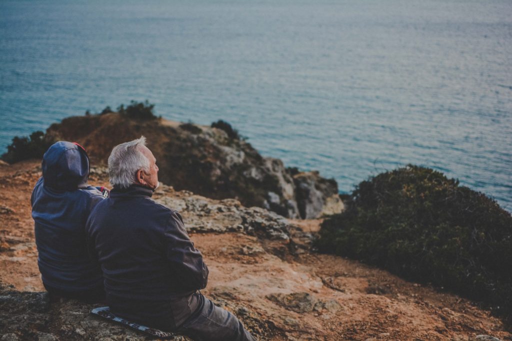 Prioritize wellness as you age; image of a man with gray hair looking out on the ocean alongside a companion in a hooded jacket